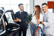 © fotofabrika - Young couple choosing a car at the dealership with manager helping