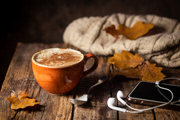 Cozy background with cup of coffee, headphones and Autumn leaves on wooden background