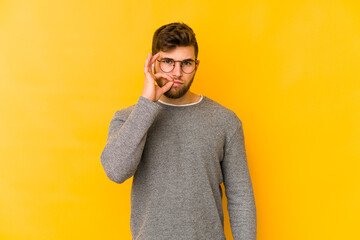 Wall Mural - Young caucasian man isolated on yellow background with fingers on lips keeping a secret.