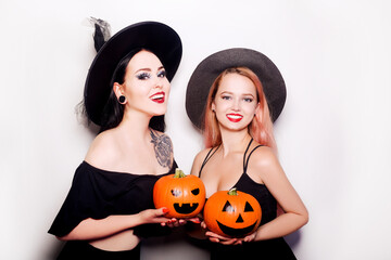 Two women witches are holding pumpkins in their hands. The women are having fun and smiling. Halloween party