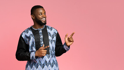 Wall Mural - Cheerful black man in traditional costume pointing at free space