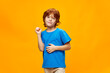 © SHOTPRIME STUDIO - Red-haired boy in a blue t-shirt gestures with his hands smile yellow background.