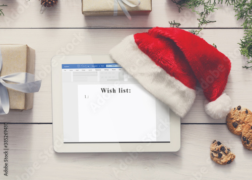 Electronic Wish List. Digital Tablet With Santa Hat, Creative Christmas Background