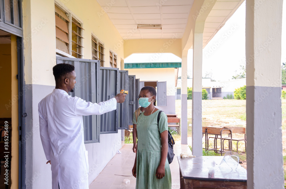 a young handsome african class teacher holding as thermometer to scan the temperature of his student before entering the classroom - obrazy, fototapety, plakaty 