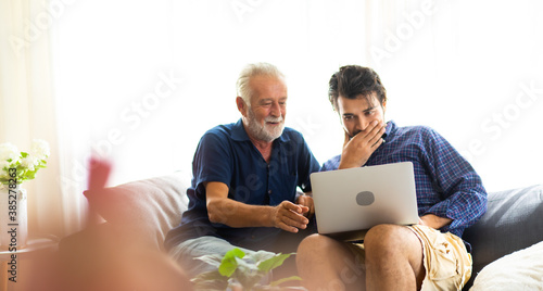 Father and son family time together at home concept. Smiling old father and happy son sitting on sofa using digital laptop computer in living room at home