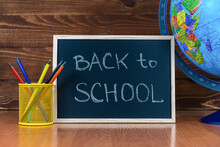 A Blackboard With Text Back To School, A Set Of Colored Pencils With A Glass And A Globe On A Wooden Background. Concept Start Of The School Year And Sale Of School Supplies. Education And Learning