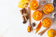 Pumpkin Puree In Different Glass Jars With Spices And Fresh Pumpkins. Autumn Or Winter Food. Light Stone Background.