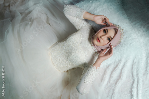Obraz Dibond Beautiful asian muslim woman in white wedding gown lying on bed. bridal wedding concept