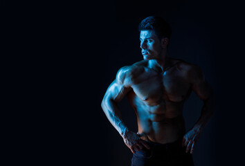 Muscular model sports young man on dark background. Fashion portrait of strong brutal guy. Sexy torso. Male flexing his muscles.