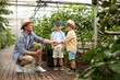 © Roman - the guide man conducts an introductory lecture for children in the garden or greenhouse, kids listen to his talk with interest, ask questions about fruits and trees, plants around them