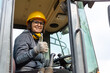 © Nenad - cheerful female excavator operator on construction site. Woman construction apprentice learning to drive heavy equipment