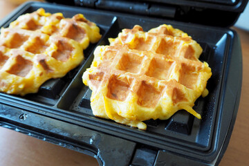 side view of two fresh round Belgian waffles made from cornmeal, eggs and pumpkin lying in a waffle iron while cooking . gluten-free homemade food