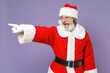 © ViDi Studio - Angry Santa Claus man in Christmas hat red suit coat white gloves glasses point index finger aside swearing screaming isolated on violet background. Happy New Year celebration merry holiday concept.