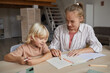 © AnnaStills - Young teacher pointing at note book and teaching the child to new subject at the table at home
