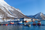 Fototapeta Góry - Lofoten islands, Senja island, Norway. Fishing harbour, parked colourful boats, snowy mountains in the background. Travel Norway.