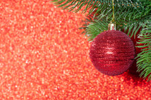 Red Shiny Ball On A Branch Of A Christmas Tree On A Red Blurred Background, Mock Up.