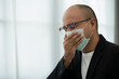 © Chanakon - Young businessman wearing a protection mask is sneezing. He had a sore throat and fever raised both hands and covered his mouth when sneezing.