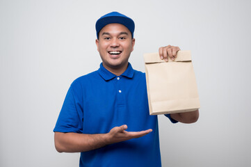 Young smiling asian delivery man in blue uniform holding paper bag food delivery on isolated white background..