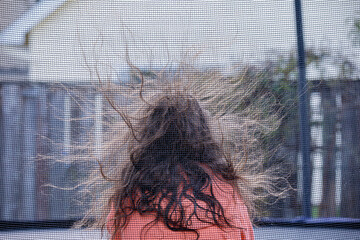 A girl sitting inside a trampoline with a netted barrier. Static electricity rising hair up in the air 