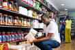 © JackF - Focused cheerful muscular African man choosing sports nutrition products in shop, reading content label