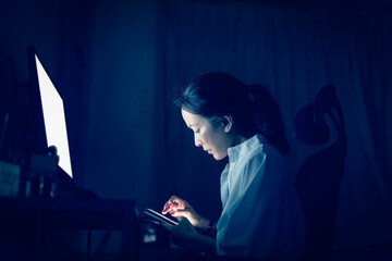 Businesswoman using cell phone while working on the computer late at night.