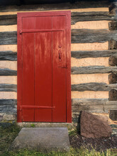 Red Wooden Door With Long, Old Style Hinges In An Early American Log Cabin On The Daniel Boone Homestead.