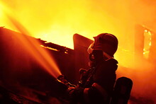 A Firefighter Sprays Water From A Hose Into A Flames During A Night Fire