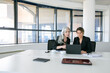 © Mangostar - Serious business ladies watching and discussing content on laptop while sitting at table with cups of coffee in meeting room. Wide shot. Teamwork and communication concept