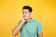 © Irene - Young handsome man wearing green casual t-shirt over isolated yellow background touching mouth with hand with painful expression because of toothache or dental illness on teeth
