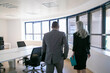 © Mangostar - Male CEO and female assistant wearing suits, walking in meeting room. Woman holding folder. Back view. Business communication concept