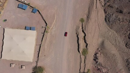 Wall Mural - Red SUV on a desert path, high altitude aerial follow footage.