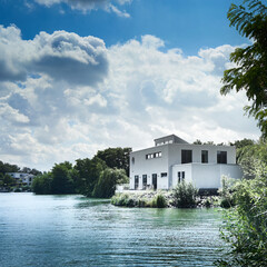 Modern white residential house on the waterfront of a crack pool with green trees and bushes