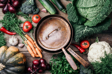 Copper pot, herbs, purple onion, pumpkin, tomato, broccoli, pepper, cabbage, carrot, parsley, calafior, zucchini on wooden background. Top view. Copy space. Banner. Autumn harvest food cooking concept