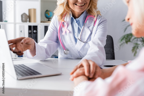 Selective focus of doctor with pink ribbon comforting patient at workplace