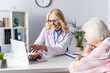 © LIGHTFIELD STUDIOS - Doctor pointing with hand and patient looking at laptop on table in clinic