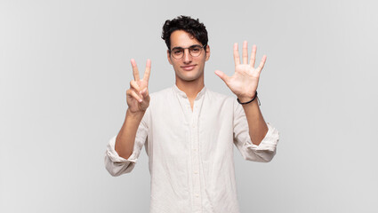 young handsome man smiling and looking friendly, showing number seven or seventh with hand forward, counting down