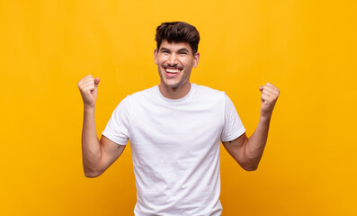 young handsome man looking extremely happy and surprised, celebrating success, shouting and jumping