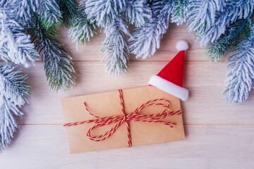 Wall Mural - Envelope with red Santa hat and frosty Christmas tree branches over wooden background