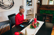 © Gerald Carter/Creative Flame - Senior Black woman sitting at table with laptop for holidays getting ready for video call