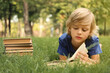 © New Africa - Cute little boy reading book on green grass in park