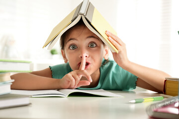 Sticker - Little girl with book on her head doing homework at table indoors