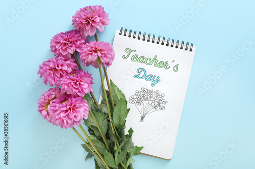 Beautiful flowers and notebook with words TEACHER\'S DAY on light blue background, flat lay