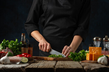 Wall Mural - Professional chef in black uniform cuts with knife parsley on chopped board for cooking filling for tacos. Backstage of preparing traditional mexican recipe. Concept of tasty food. Dark background.