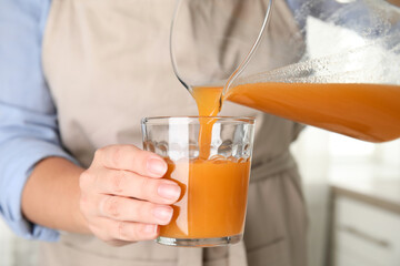 Sticker - Woman pouring freshly made carrot juice into glass in kitchen, closeup