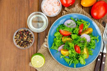 Wall Mural - Light meal of green leaves of lettuce, yellow and red tomatoes, olive oil on wooden table.