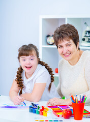 Wall Mural - A girl with down syndrome is sitting next to her mother and smiling while looking into the camera. Education for people with disabilities concept