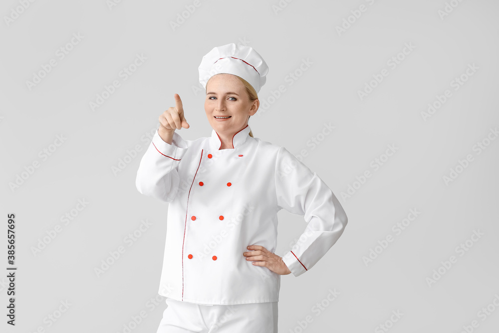 Mature female chef pointing at something on grey background