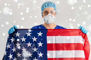 Wall Mural - medicine, healthcare and pandemic concept - young female doctor or nurse wearing goggles and face protective mask or respirator holding flag of america in winter over snow