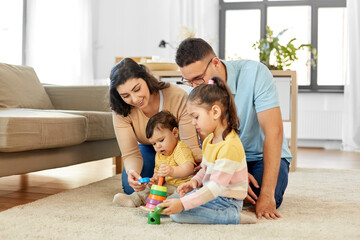 Wall Mural - family and people concept - happy mother, father, little daughter and baby son playing with pyramid toy at home