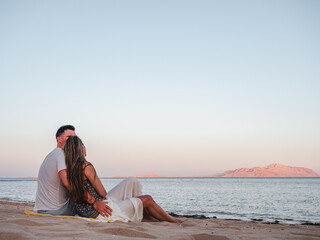 Handsome man and cute woman sitting on the beach with the sea background. Concept of leisure and travel